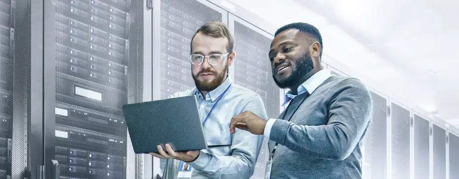 Two men looking at laptop in front of server wall